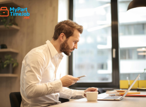 Parent using laptop at home with child nearby.